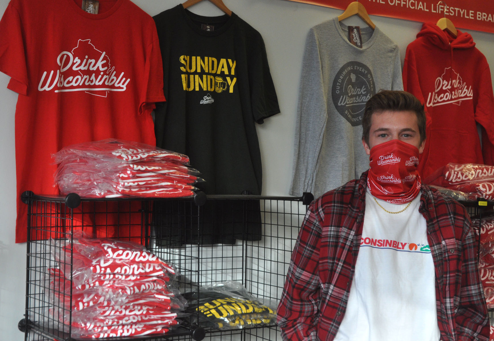 Dillon Murphy, Drink Wisconsinbly employee, stands next to some of the T-shirts that are sold at the store